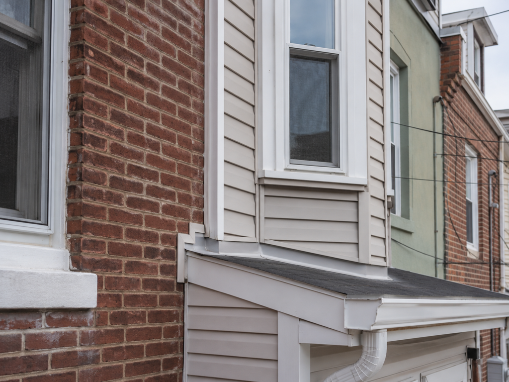 Exterior wall transition where siding meets brick masonry requiring inspection for water intrusion.
