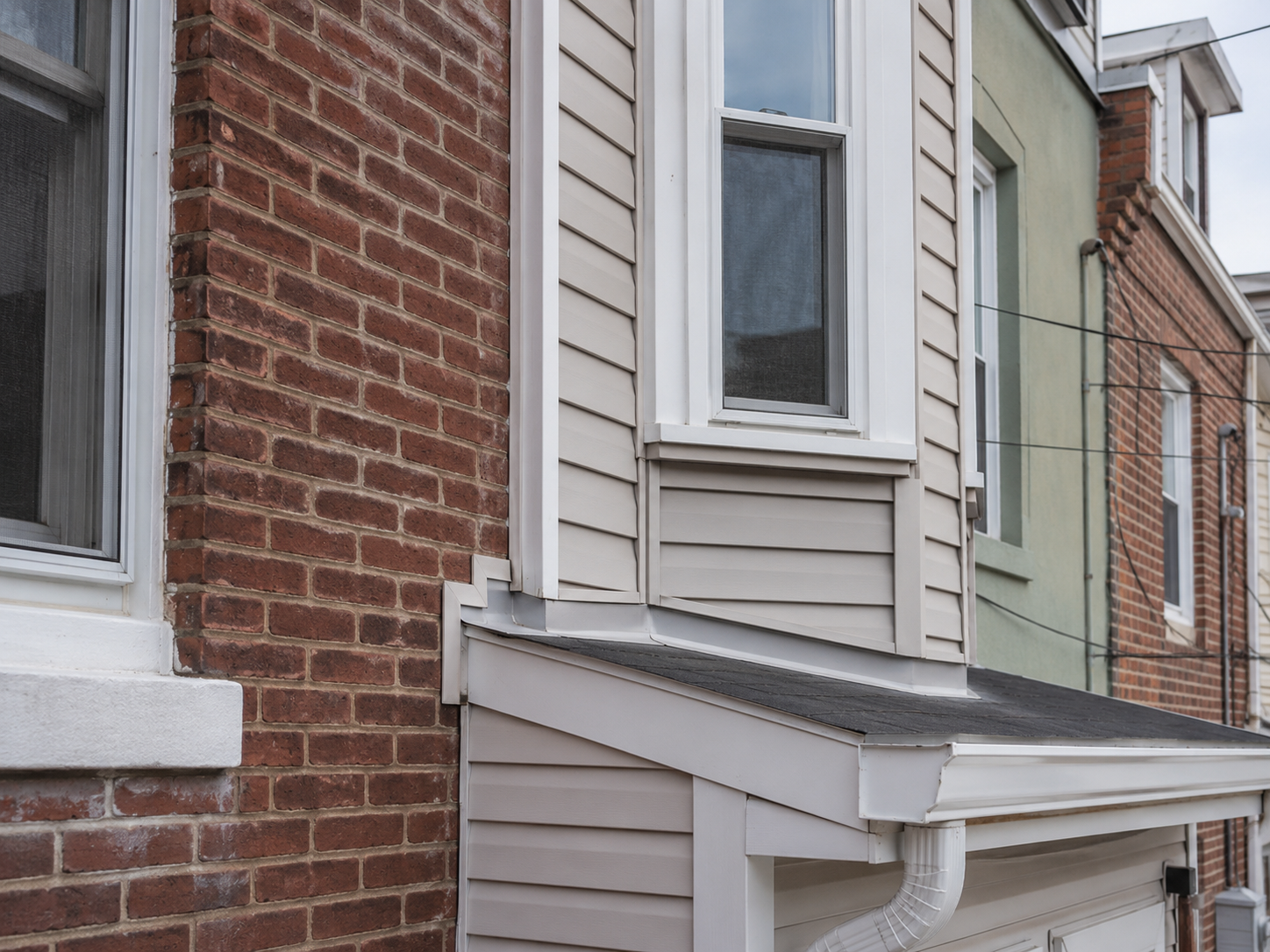 Exterior wall transition where siding meets brick masonry requiring inspection for water intrusion.